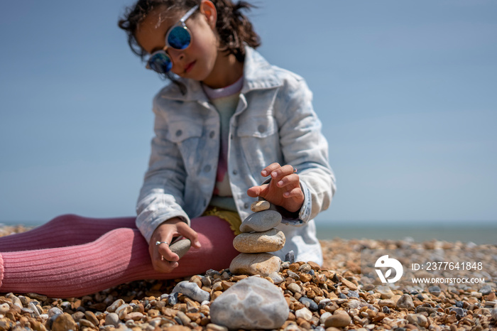 Girl (8-9) stacking stones on beach