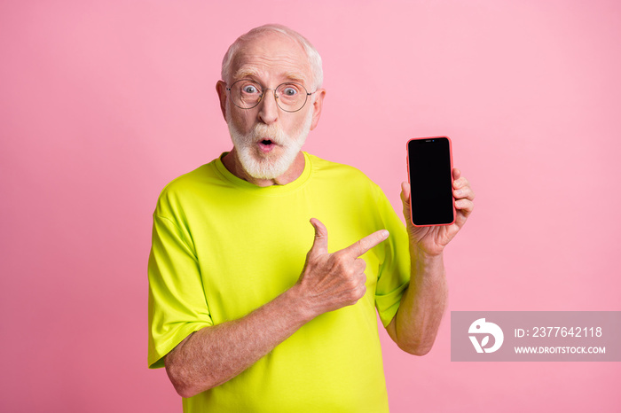 Photo of old shocked surprised amazed man wear lime t-shirt point finger at smartphone isolated on pink color background