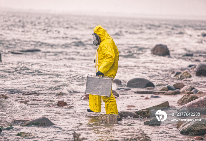 scientist in protective suit with silver case walking on rocky beach