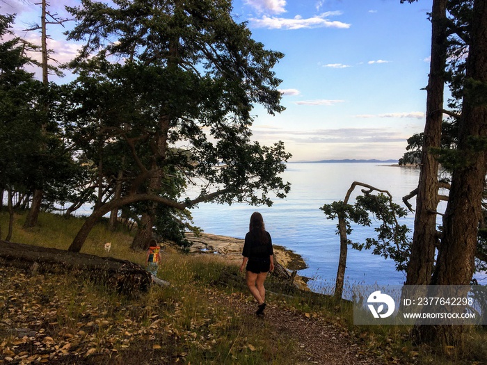 A mother and her young daughter hiking along a beautiful trail in the gulf islands during the evening, with beautiful views of the ocean in the background, in British Columbia, Canada.