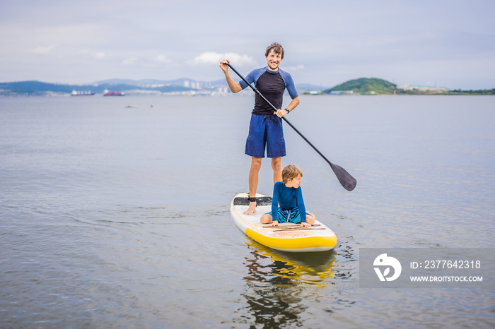 Father and son paddling on stand up board having fun during summer beach vacation