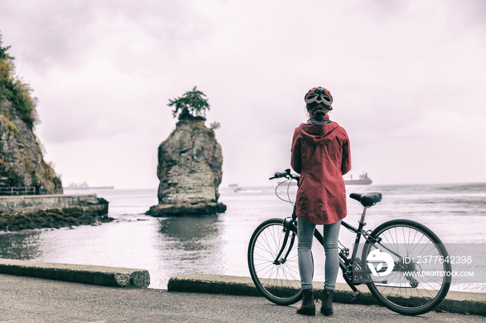 Bike girl biking on city bicycle commute in Stanley Park, Vancouver, BC British Columbia, Canada. Vancouver cyclist woman on bike path looking at Siwash rock.