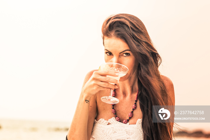 Young woman drinking a cocktail in Long Beach, at sunset. Ko Lanta, Thailand.