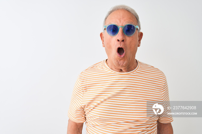 Senior grey-haired man wearing striped t-shirt and sunglasses over isolated white background afraid and shocked with surprise expression, fear and excited face.