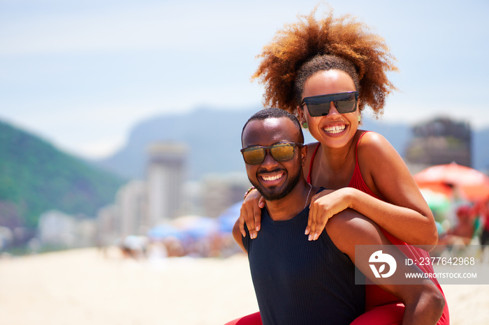 waist up portrait young black brazilian afro carioca couple in piggyback position smiling and having fun in Ipanema beach Brazil