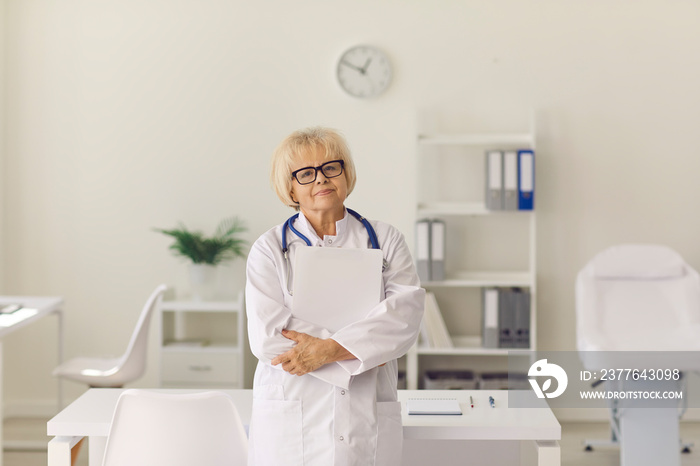 Portrait of experienced senior doctor looking at camera standing in hospital office