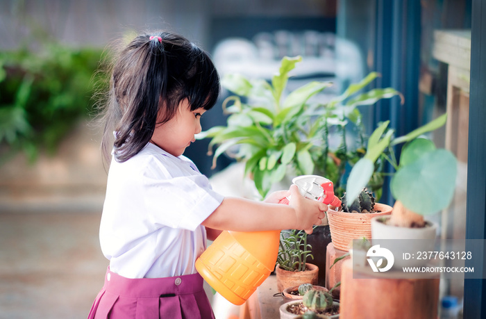 Happy Cute Asian Girl Enjoying with Gardening Activities, A Three Years old Child in Student Uniform is Watering Plant in the Garden, Happiness Moment