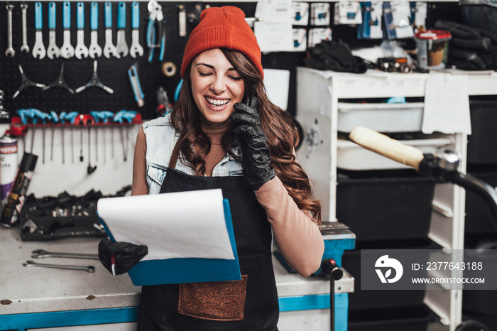 Beautiful young female mechanic talking on phone while repairing bicycles in a workshop..