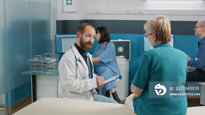 Male physician taking notes and consulting elder person in medical cabinet. Doctor and senior woman attending examination appointment to discuss alternative medicine for health care.