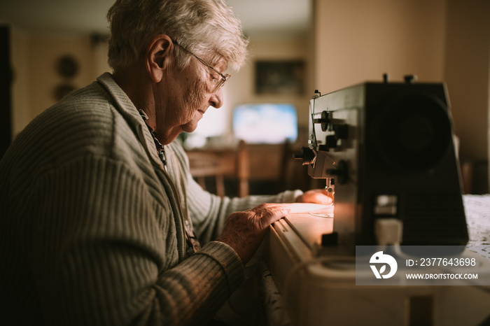 Senior sweet grandmother sews clothes on a sewing machine in the living room.