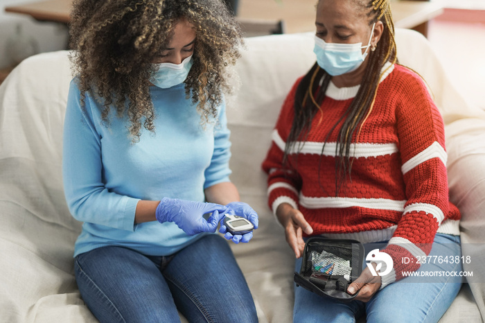 Young african american nurse doing blood sugar diabetes test to african senior woman patient at home for coronavirus outbreak