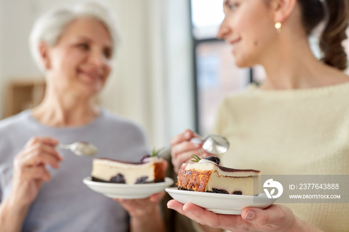 family, generation and people concept - happy smiling senior mother and adult daughter eating cake at home