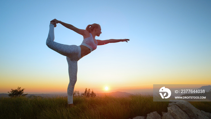 AERIAL: Flexible Caucasian woman holds a scorpion pose in front of the sunset.