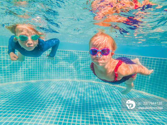 Kids having fun playing underwater in swimming pool on summer vacation