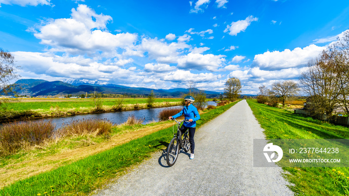 Senior woman biking along the Alouette River on the dyke surrounding Pitt Polder at the town of Maple Ridge in British Columbia, Canada