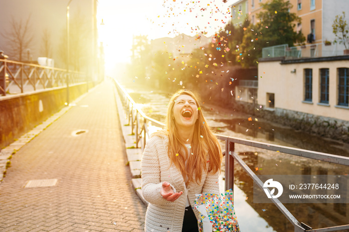 Happy young woman playing with confetti on street