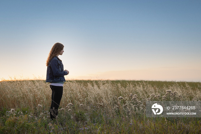 Young woman in field praying with hands folded together at sunset with copy space