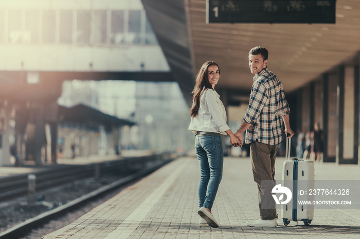 Full length portrait of cheerful female speaking with glad man while holding arms together. They walking on platform. He keeping baggage