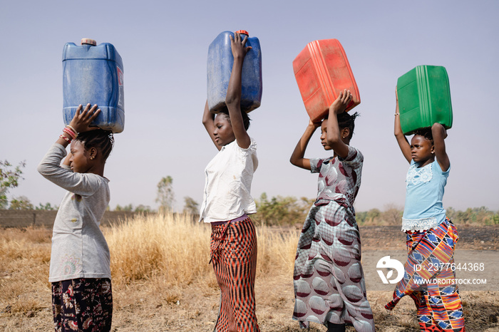 Four African girls marching in a line with colored canisters on their heads, symbolising that fetching water is a girl thing