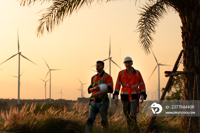 Engineers working on wind farms for renewable energy are responsible for maintaining large wind turbines. Returning from work during while the evening sun shines a beautiful golden light upon both of