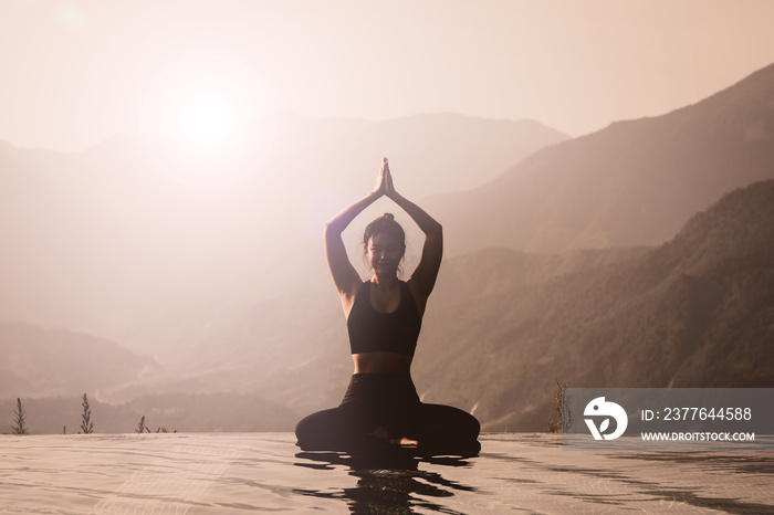 Beautiful Asian woman practice yoga Lotus pose on the pool above the Mountain peak in the morning in front of beautiful nature views,Feel so comfortable and relax with yoga in holiday,Warm tone