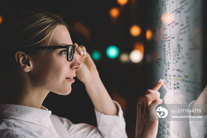 Digital monitor with public transport subway map. Female standing at big display with advanced innovative technology. Young woman touching with finger sensitive screen while selecting surface option