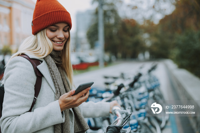 Young girl using gadget for rental bike in city