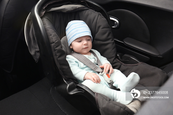 Cute baby boy sitting in safety car seat