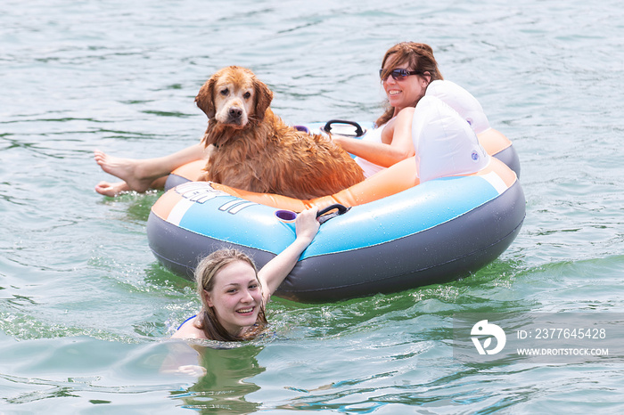 Happy teenage daughter pulling Mom and dog on inflatable tube