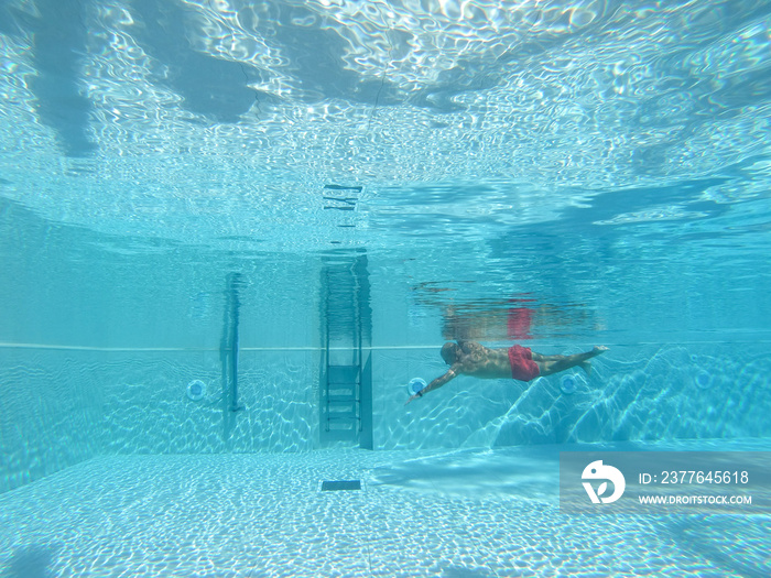 underwater scene of a man swimming  crawl sltyle in a blue crystal clear watter swimming pool. Concept of sport, holiday and travel.