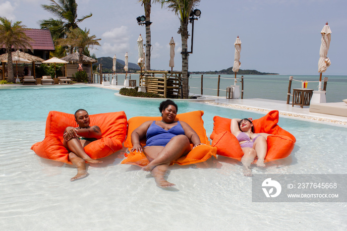 Group of cheerful women relaxing on pool rafts in swimming pool