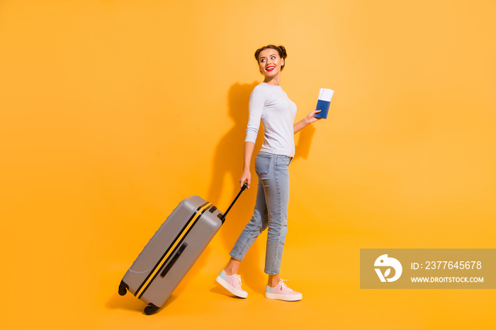 Profile side full length body size photo of cute lady going perfect voyage abroad explore sightseeing holding suit-case documents hands isolated yellow shadow background in white denim jeans clothes