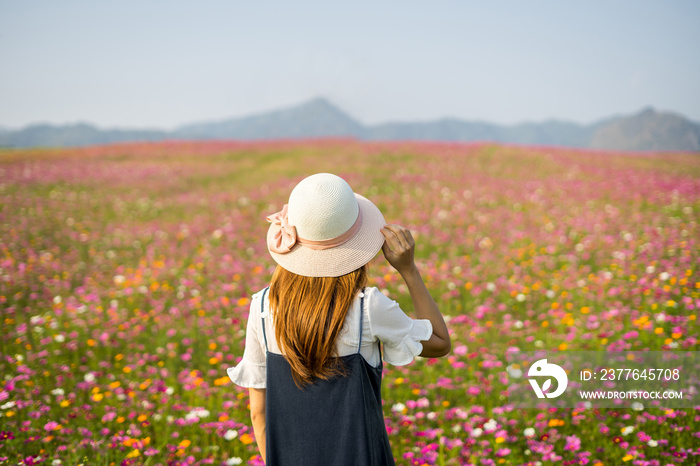 Young woman traveler standing and looking beautiful blooming flowers field