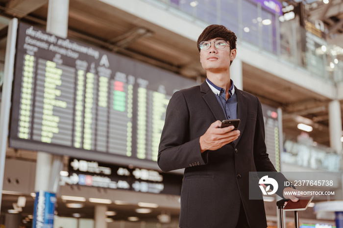 Businessman standing at time flight schedule billboard hold the smartphone at airport terminal gate.