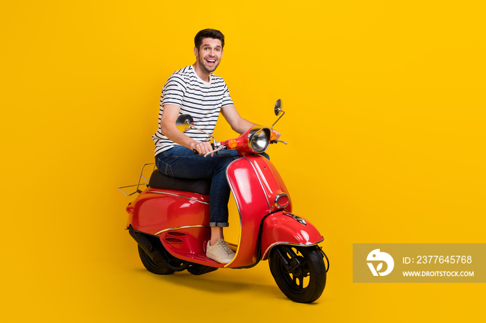 Full length photo of pretty impressed guy dressed striped t-shirt riding moped empty space isolated yellow color background