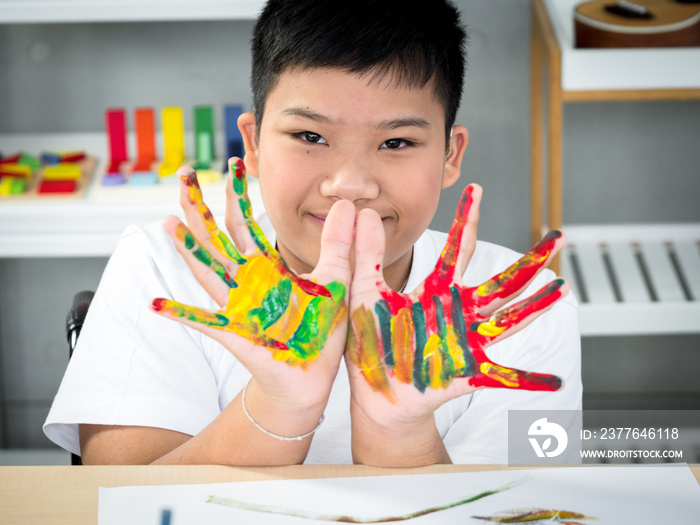 Portrait of disabled child in the wheelchair is showing his hands painted proudly in the spacial classroom.