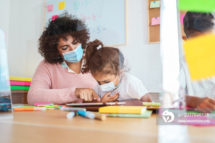 Teacher using tablet with children in preschool during coronavirus outbreak - Back to school and covid-19 lifestyle - Focus on woman’s hand