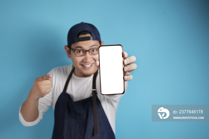 Portrait of Asian male chef or waiter looks happy and proud showing empty copy space smart phone, presenting blank phone template