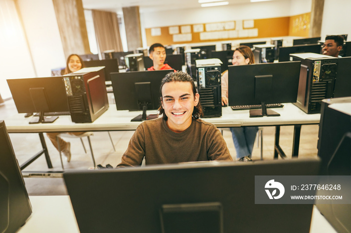 Young students using computers inside technology class at school room - Focus on center guy face