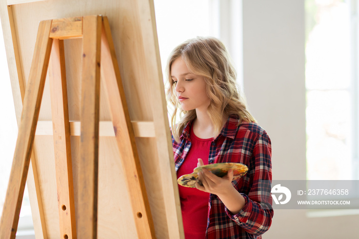 student girl with easel painting at art school