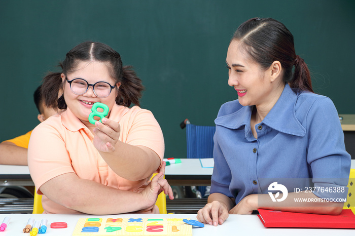 Asian disabled children Or, an autistic child learns to read, write and train their hand and finger muscles with a teacher at their classroom desk.