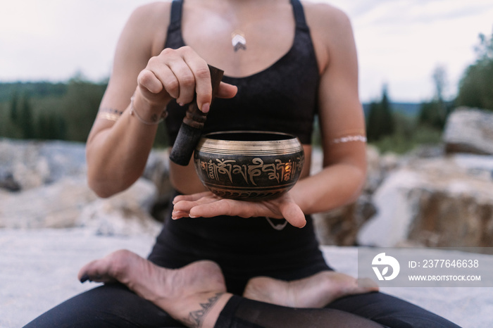 Yogi girl in black suit playing tibetan bowl in marble quarry