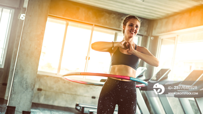 Woman doing exercises with hula hoop in gym.