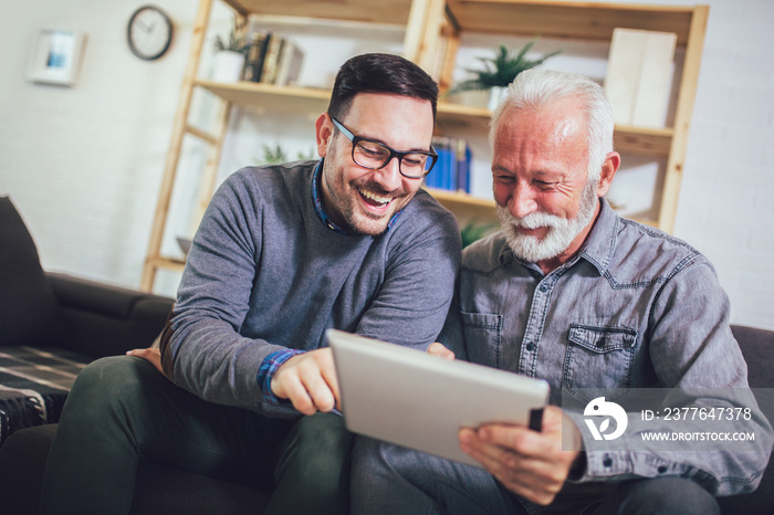 Portrait of senior man with adult son using digital tablet at home