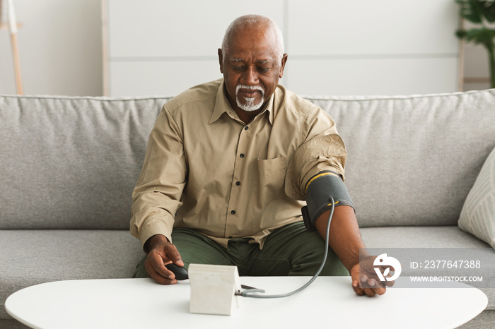 Senior Black Male Measuring Blood-Pressure With Sphygmomanometer Device At Home