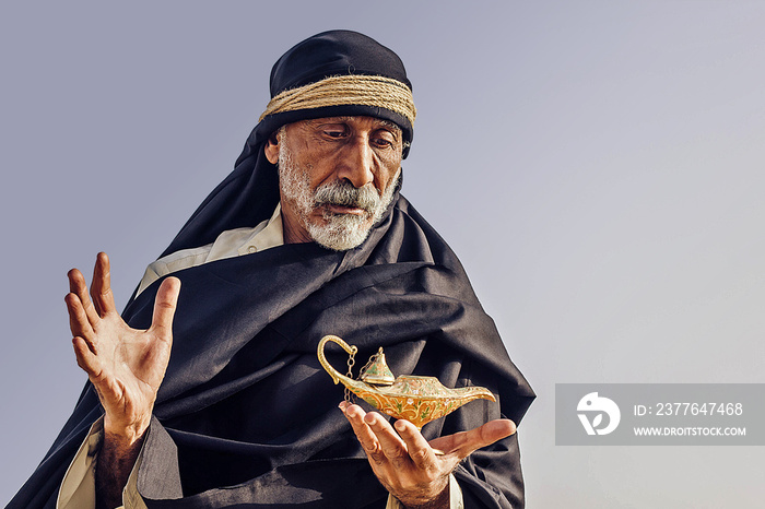 An old Arabic sorcerer holds an Aladdin’s lamp and conjures.