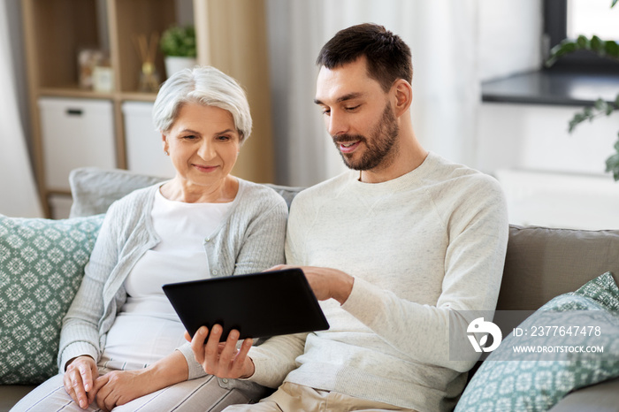 family, technology and people concept - adult son teaching his senior mother how to use tablet computer at home