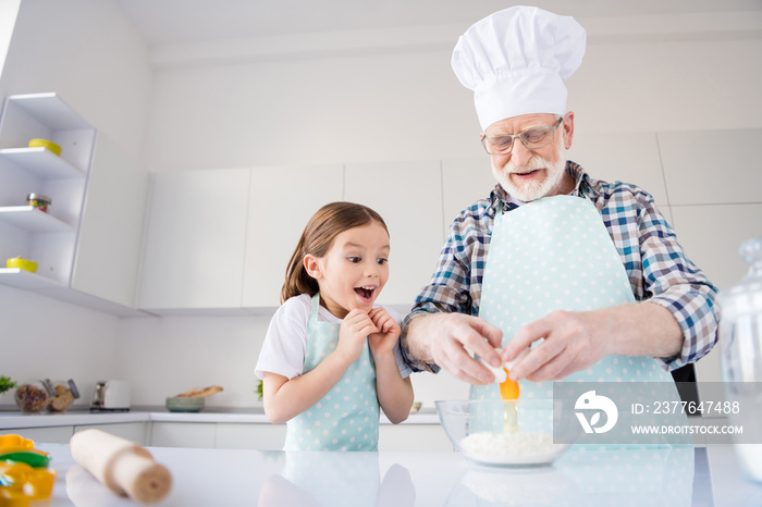 Photo of little girl granddaughter watching how aged grandpa breaking eggs make dough best friends baking cake cookies together prepared ingredients weekend home kitchen indoors