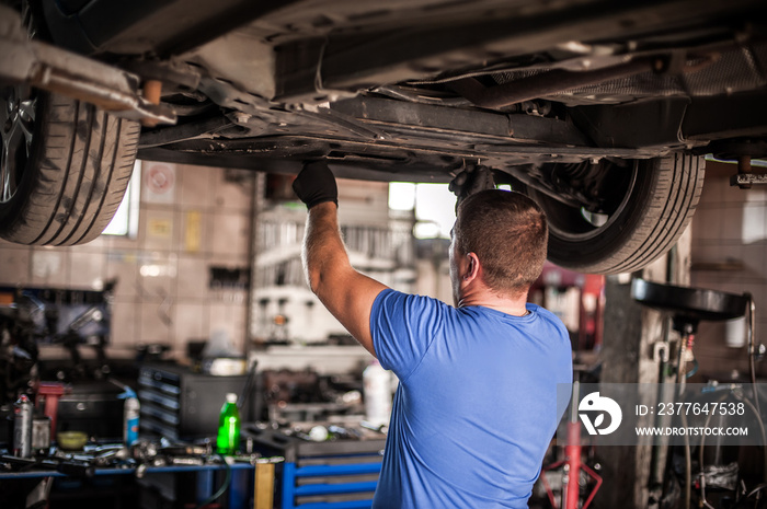 Auto mechanic repairer checking condition under car on vehicle lift