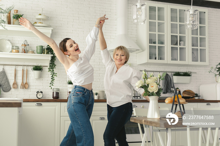 Mother and her adult daughter are having fun and dancing in the kitchen